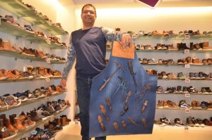 Peter Ligtvoet laat een nagemaakte lederen schoenmakersschort zien waarop handwerktuigen van zijn opa zijn bevestigd. De schort is een van de voorwerpen die tijdens WieKentKunst in de winkel wordt geëxposeerd.