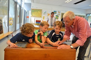 Op de onderwijsexpositie in De Vonder krijgen kinderen uit het digitale tijdperk van ‘mister’ Jacques van Rijswijk les in het schrijven met een griffel op een leitje.(Foto: Paul Spapens)